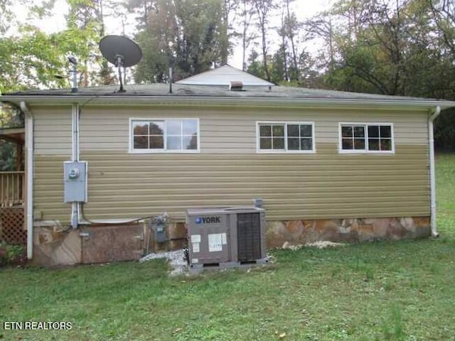 rear view of property with central AC unit and a lawn