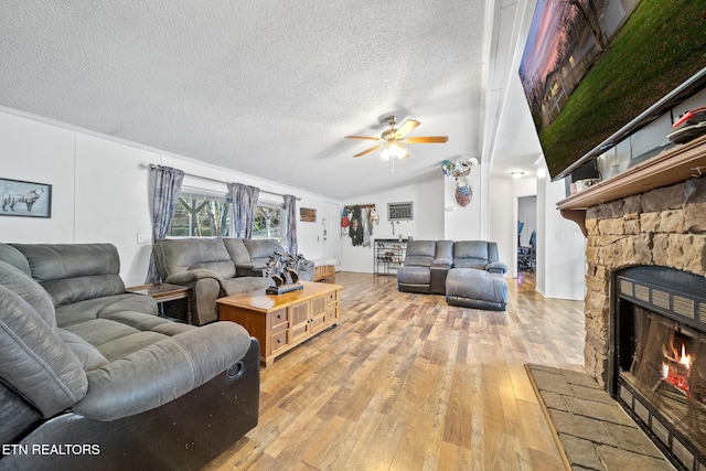 living room featuring a stone fireplace, vaulted ceiling, ceiling fan, a textured ceiling, and light hardwood / wood-style floors