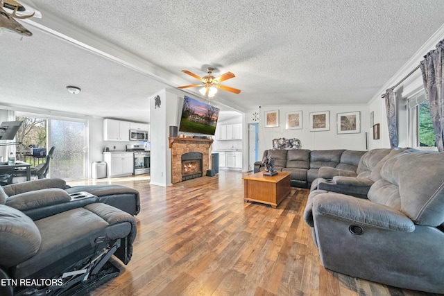 living room featuring lofted ceiling, ceiling fan, a fireplace, a textured ceiling, and wood-type flooring