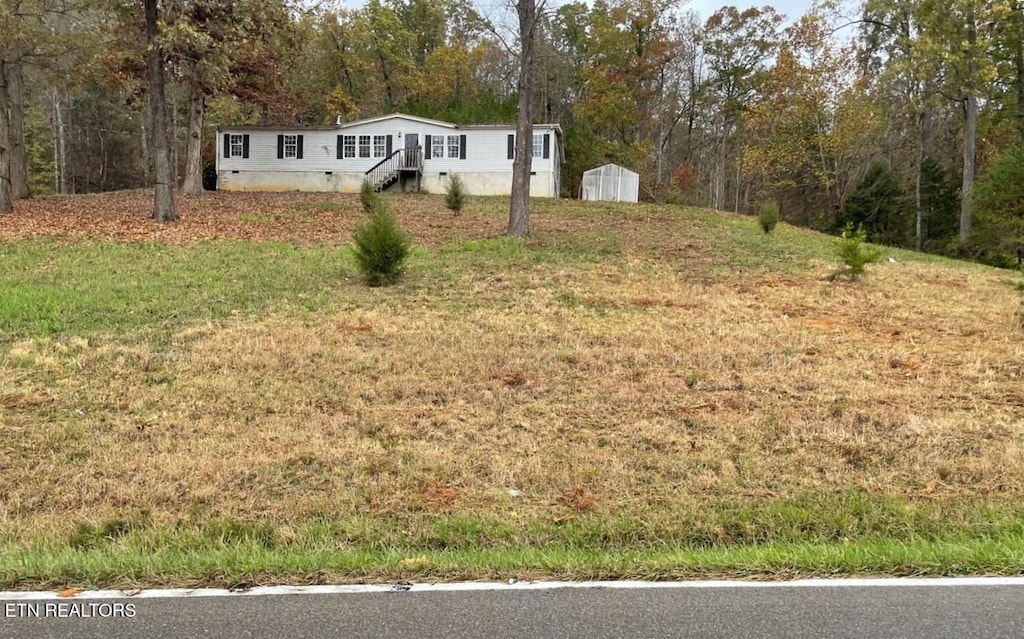 view of front of property featuring an outbuilding, a storage shed, a front yard, crawl space, and a wooded view