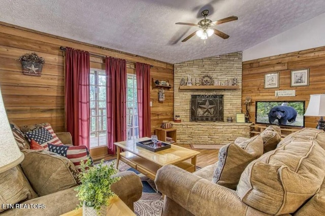 living room with a textured ceiling, vaulted ceiling, wooden walls, hardwood / wood-style floors, and a stone fireplace