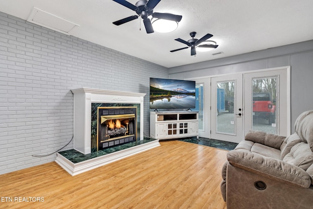 living room with brick wall, a textured ceiling, ceiling fan, hardwood / wood-style flooring, and a premium fireplace