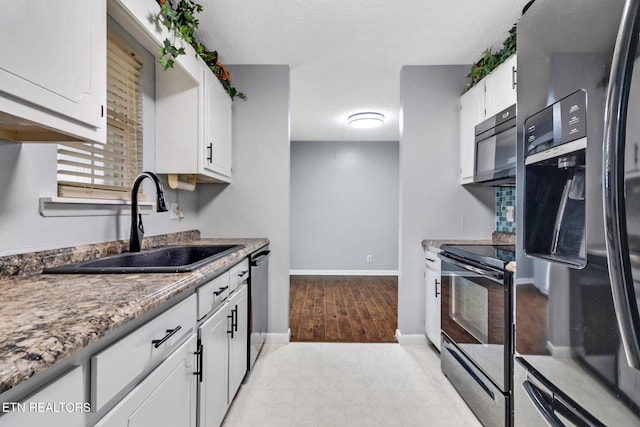 kitchen with stone counters, black appliances, white cabinets, sink, and light wood-type flooring