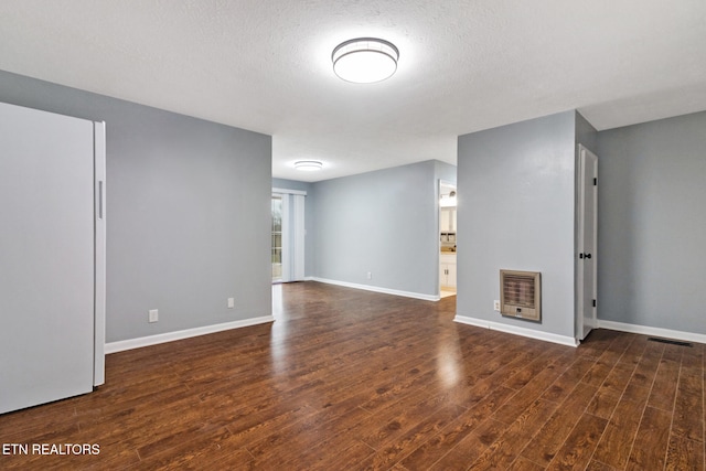 unfurnished room with a textured ceiling, dark hardwood / wood-style floors, and heating unit