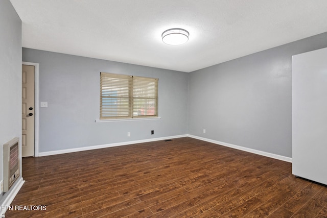 spare room with dark hardwood / wood-style flooring, a textured ceiling, and heating unit