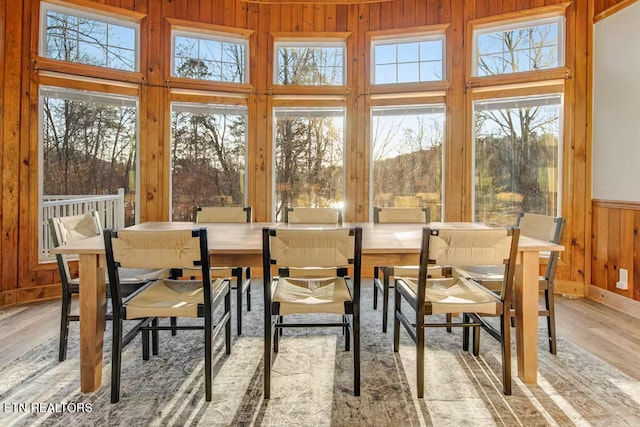 dining area with wood walls, light hardwood / wood-style flooring, and a towering ceiling