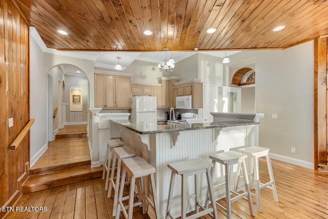 kitchen featuring dark stone countertops, light brown cabinets, light hardwood / wood-style floors, and white appliances