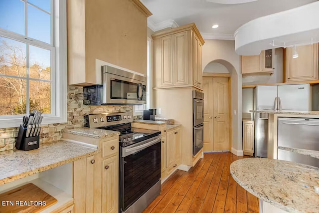 kitchen with light stone countertops, crown molding, light wood-type flooring, and appliances with stainless steel finishes