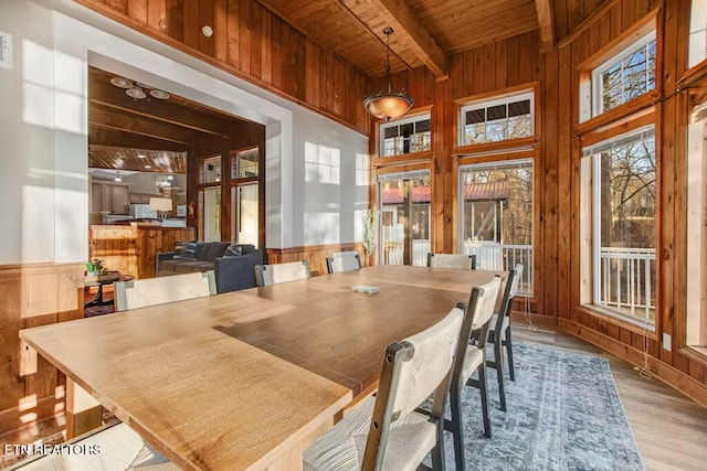 dining room with wood walls, light hardwood / wood-style flooring, beamed ceiling, and wood ceiling