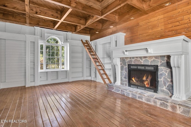 unfurnished living room with hardwood / wood-style floors, wood walls, wooden ceiling, a stone fireplace, and beam ceiling