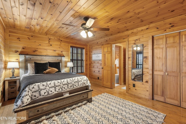 bedroom featuring ceiling fan, light hardwood / wood-style floors, wooden walls, and ensuite bath