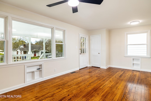 empty room with visible vents, wood-type flooring, baseboards, and built in shelves