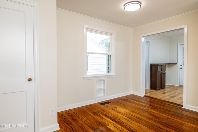 spare room with visible vents, baseboards, wood finished floors, and ornamental molding