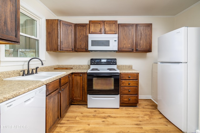 kitchen with white appliances, light wood finished floors, ornamental molding, a sink, and light countertops