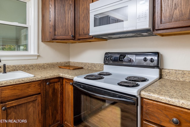 kitchen with a sink, light countertops, white microwave, and range with electric cooktop