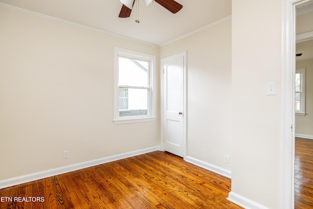 empty room featuring ceiling fan, baseboards, wood finished floors, and ornamental molding