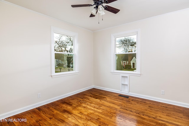 empty room featuring crown molding, wood finished floors, baseboards, and visible vents