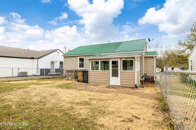 back of house with metal roof, a yard, central AC, and a fenced backyard