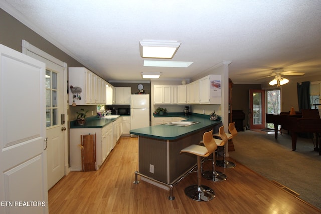 kitchen with kitchen peninsula, light hardwood / wood-style floors, a breakfast bar, white cabinets, and white fridge