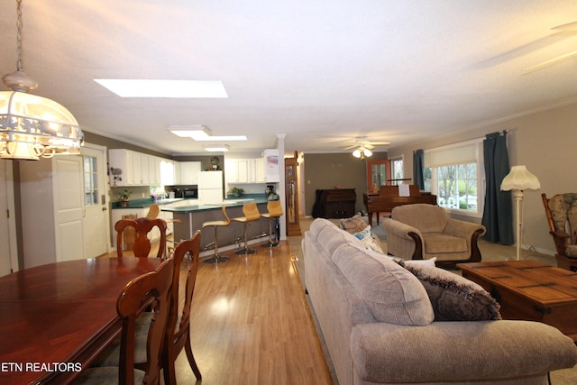 living room featuring ceiling fan, light hardwood / wood-style floors, ornamental molding, and a skylight