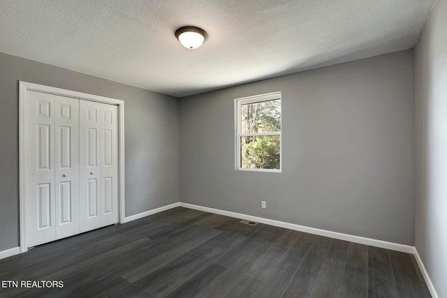 unfurnished bedroom featuring dark hardwood / wood-style floors, a textured ceiling, and a closet