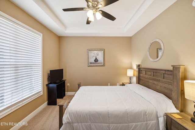 bedroom with light carpet, a tray ceiling, and ceiling fan