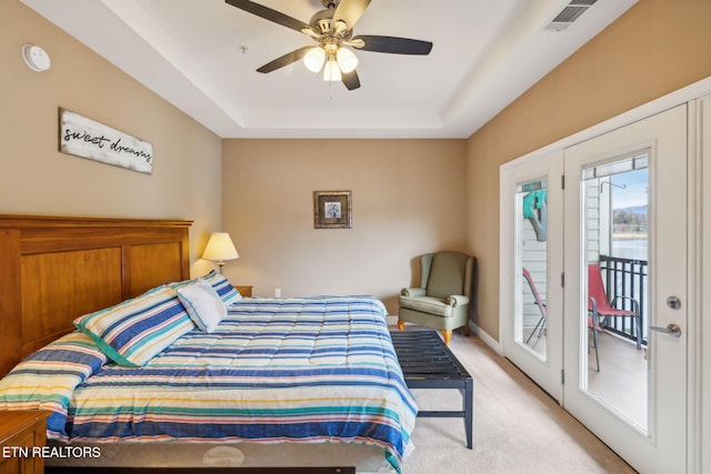 bedroom with access to exterior, light carpet, a tray ceiling, and ceiling fan