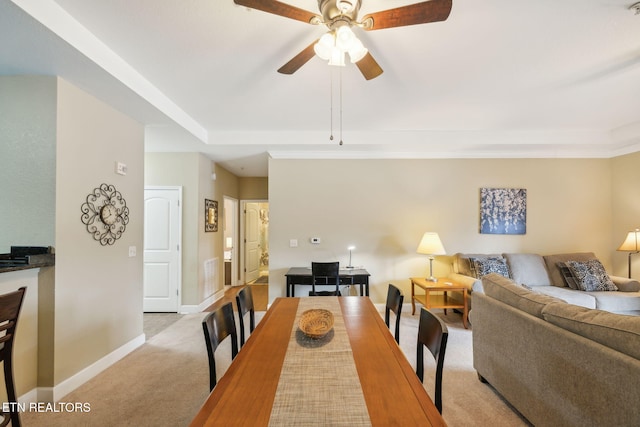 carpeted dining room featuring a raised ceiling and ceiling fan