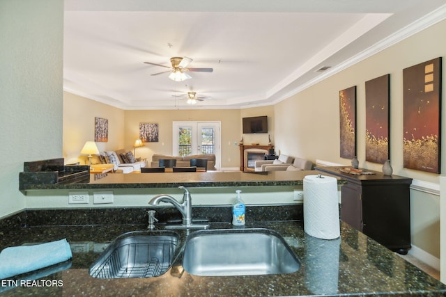 kitchen with a raised ceiling, sink, crown molding, ceiling fan, and dark stone countertops