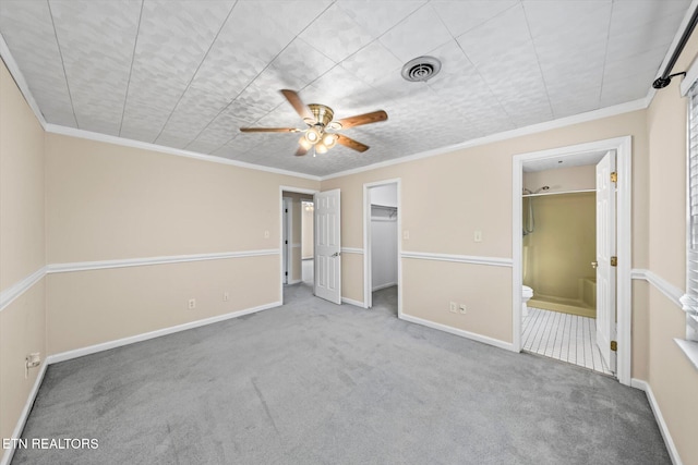 unfurnished bedroom featuring carpet, a walk in closet, crown molding, ceiling fan, and connected bathroom