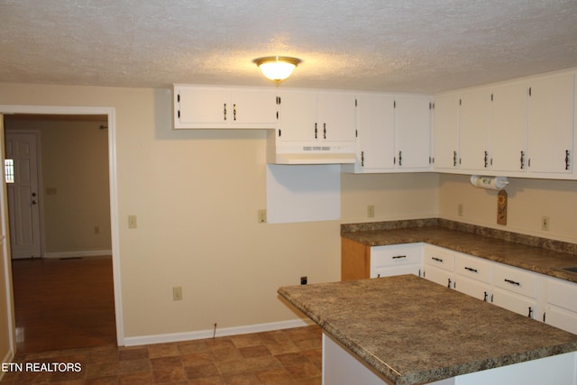 kitchen with a textured ceiling, white cabinetry, and dark stone counters