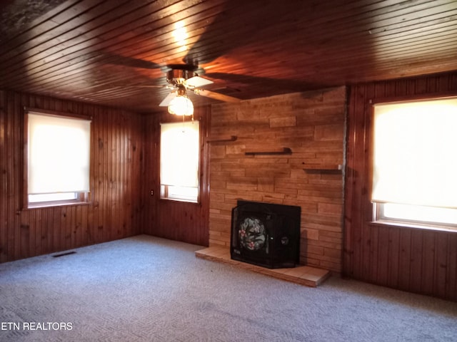 unfurnished living room with wooden walls, carpet flooring, wooden ceiling, and a wealth of natural light