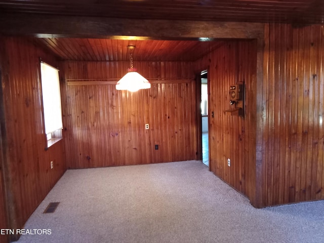 empty room featuring carpet floors, wood walls, and beamed ceiling