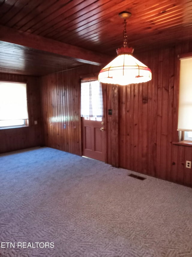 empty room with beamed ceiling, wood walls, and carpet floors