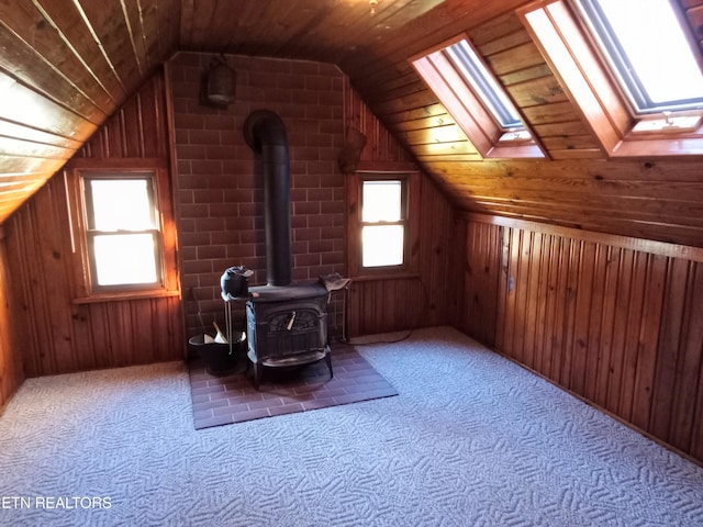 additional living space with a wood stove, wooden ceiling, a healthy amount of sunlight, and lofted ceiling with skylight