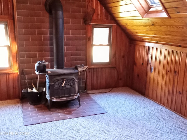 additional living space featuring a wood stove, brick wall, wood walls, vaulted ceiling with skylight, and carpet