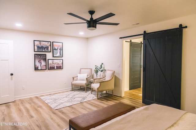 sitting room featuring ceiling fan, a barn door, and light wood-type flooring