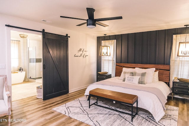 bedroom featuring ceiling fan, a barn door, light wood-type flooring, and connected bathroom