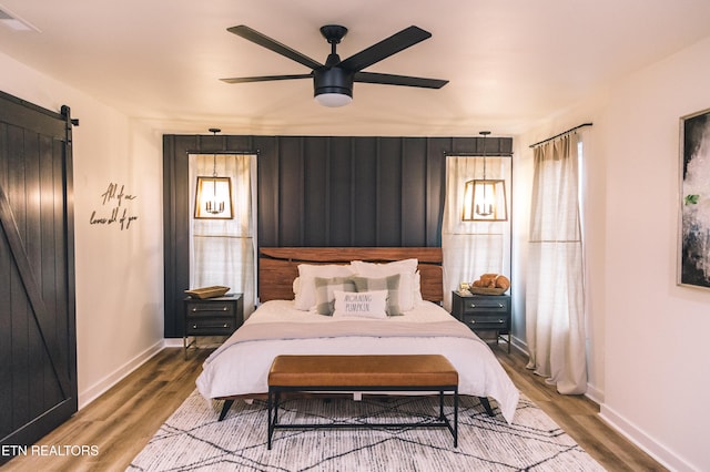 bedroom featuring hardwood / wood-style flooring, ceiling fan, a barn door, and multiple windows