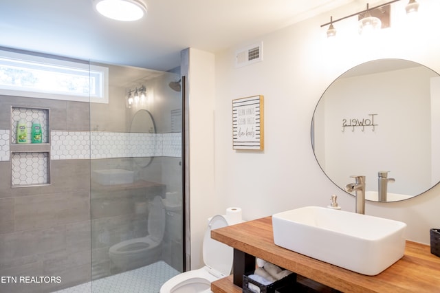 bathroom with a tile shower, toilet, and sink