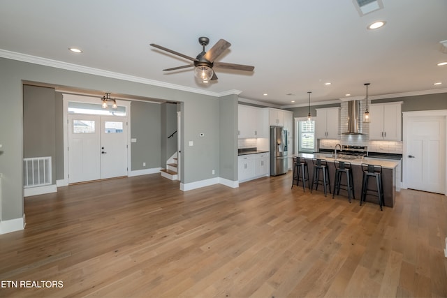 kitchen with stainless steel refrigerator with ice dispenser, a center island with sink, white cabinetry, and decorative light fixtures