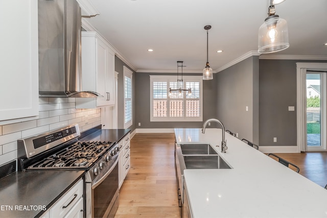 kitchen featuring stainless steel gas range oven, white cabinets, sink, light wood-type flooring, and decorative light fixtures