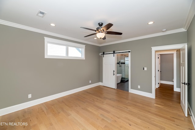 unfurnished bedroom featuring ceiling fan, a barn door, ornamental molding, and light hardwood / wood-style flooring