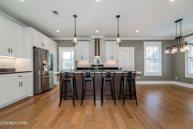 kitchen featuring white cabinets, stainless steel fridge with ice dispenser, light wood-type flooring, and wall chimney range hood