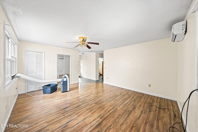 interior space with wood-type flooring, a textured ceiling, a wall unit AC, and ceiling fan