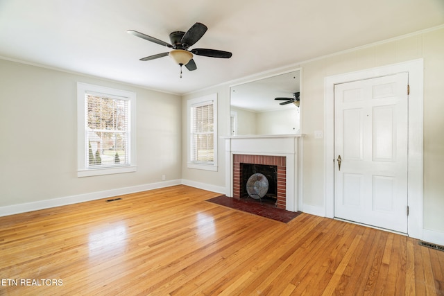 unfurnished living room featuring ceiling fan, light hardwood / wood-style floors, ornamental molding, and a brick fireplace