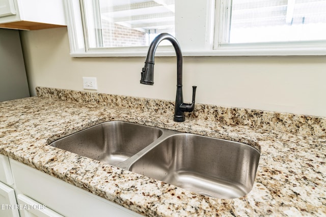 details with white cabinets, light stone counters, and sink