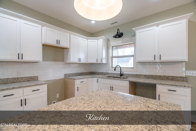 kitchen featuring backsplash, light stone countertops, white cabinetry, and sink