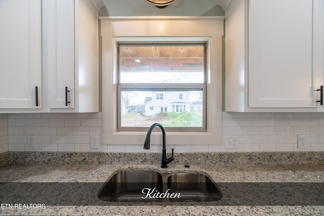 kitchen featuring light stone countertops, tasteful backsplash, white cabinetry, and sink