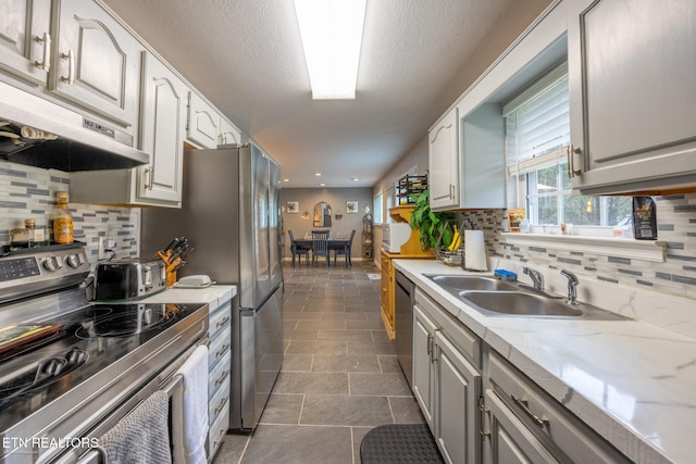 kitchen with decorative backsplash, sink, light stone countertops, and appliances with stainless steel finishes